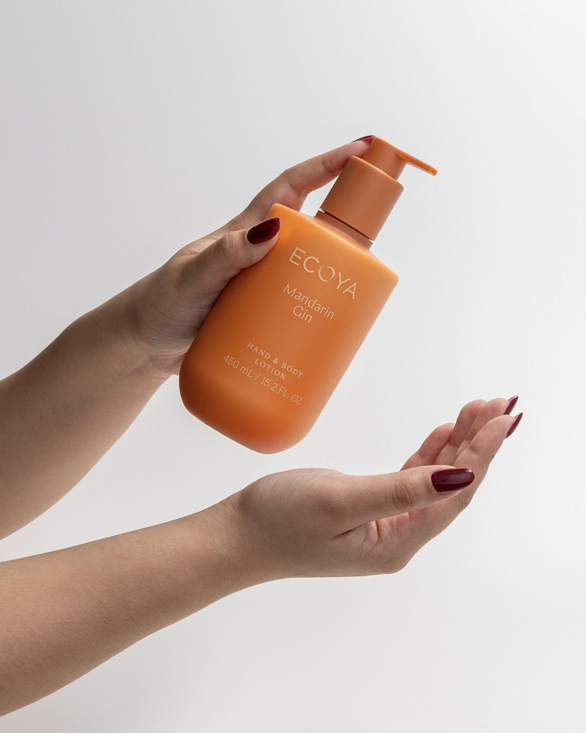 Hand holding an orange Ecoya hand and body lotion bottle against a plain background
