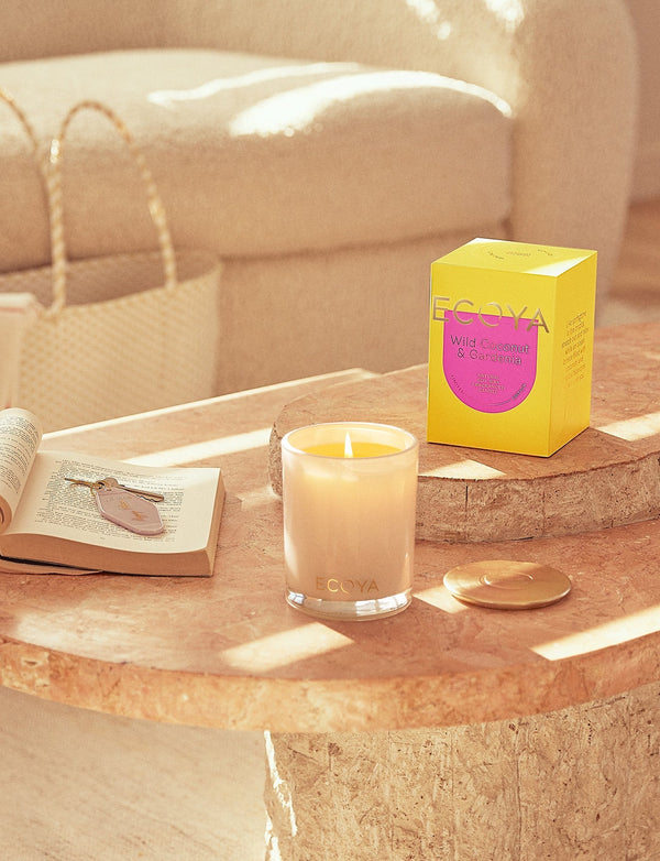 An Ecoya Sensory Escapes: Wild Coconut & Gardenia Madison Candle, a fragrant and beautifully designed gift, adorns a living room table.