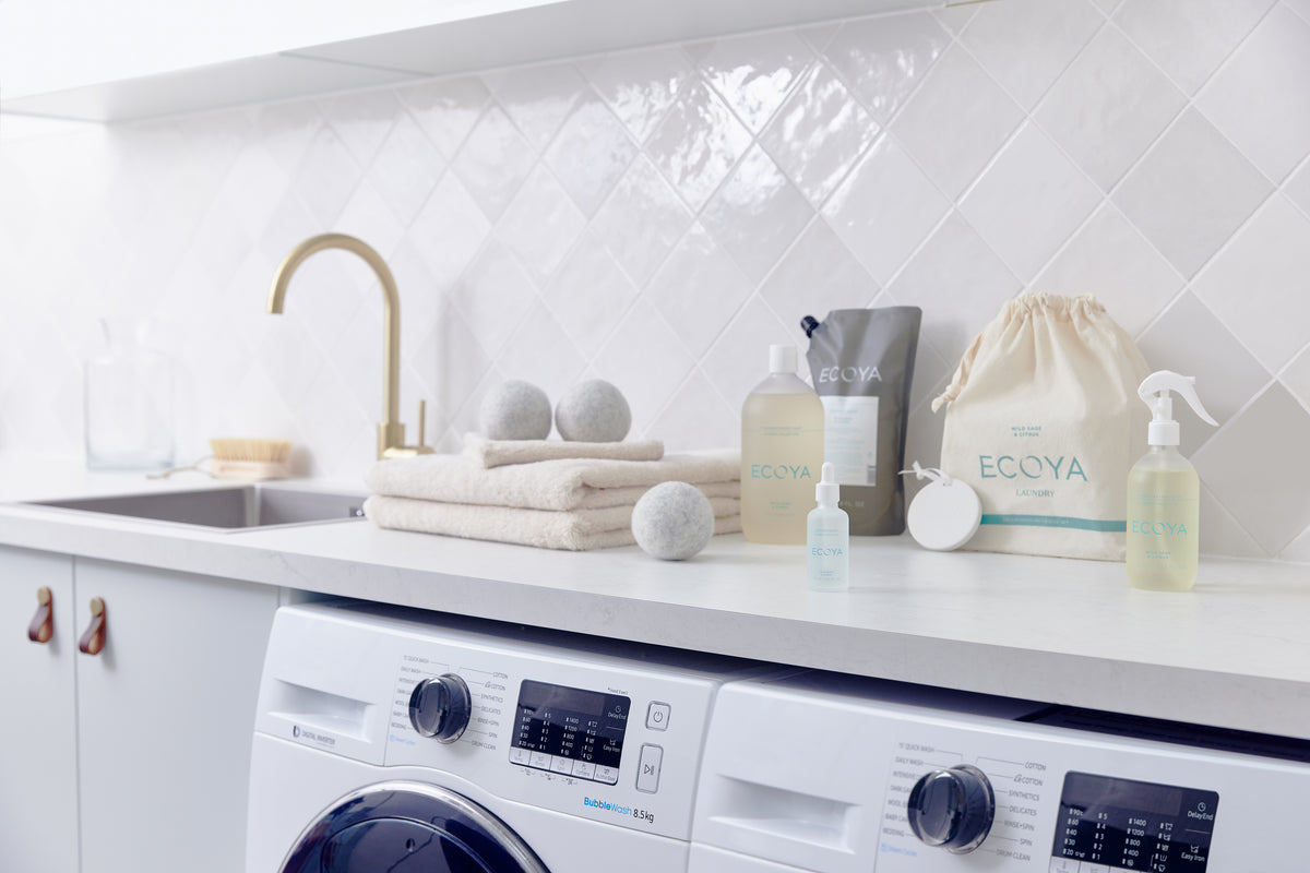 Laundry room bench styled with Ecoya laundry liquid, wool dryer balls, towels and a linen bag