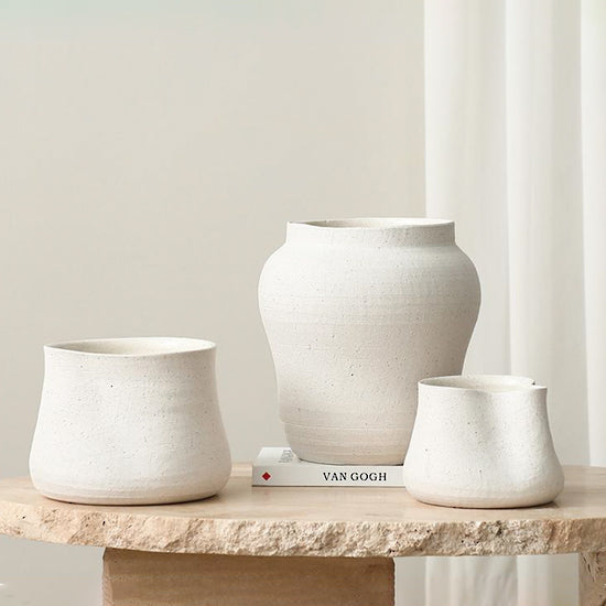Three Sandface vessels grouped on a travertine plinth, pinched pots either side of the bellied vase
