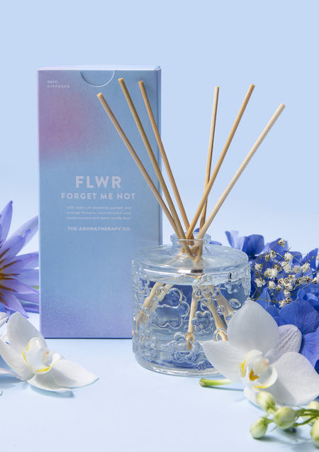 The Forget Me Not diffuser beside its blue carton with white orchids and blue petals