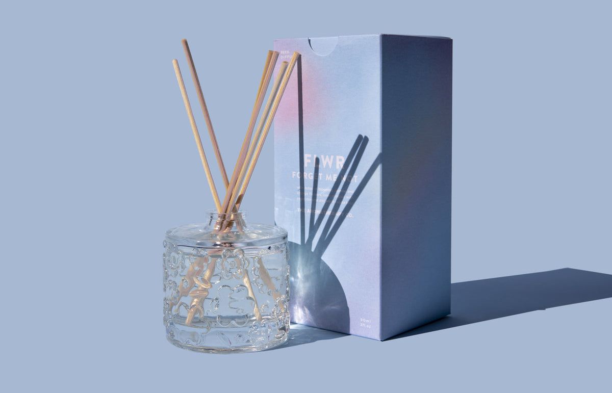 The Forget Me Not diffuser beside a deep blue gift box on a blue grey backdrop
