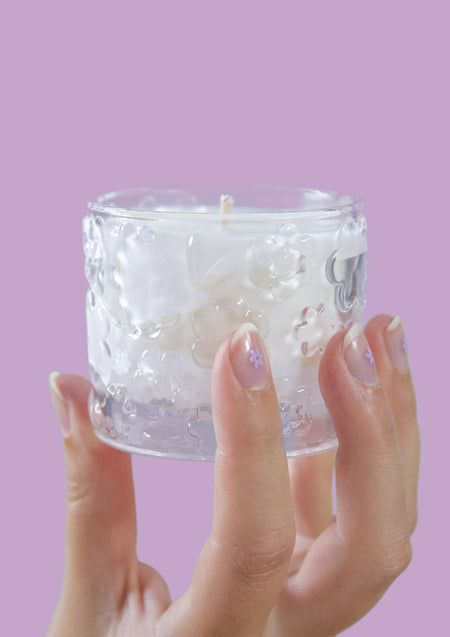Two hands holding the FLWR Sugared Rose candle against a lilac backdrop