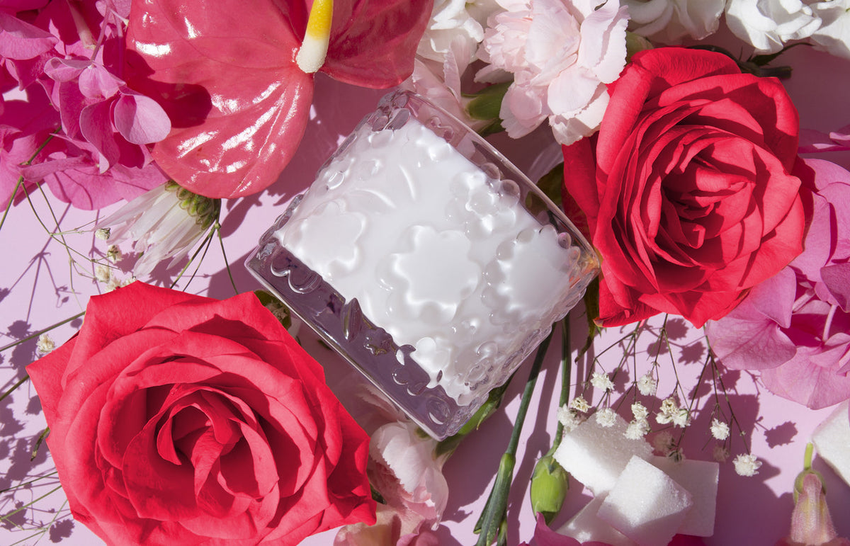 The Sugared Rose candle on its side among red roses, pink anthurium and sugar cubes