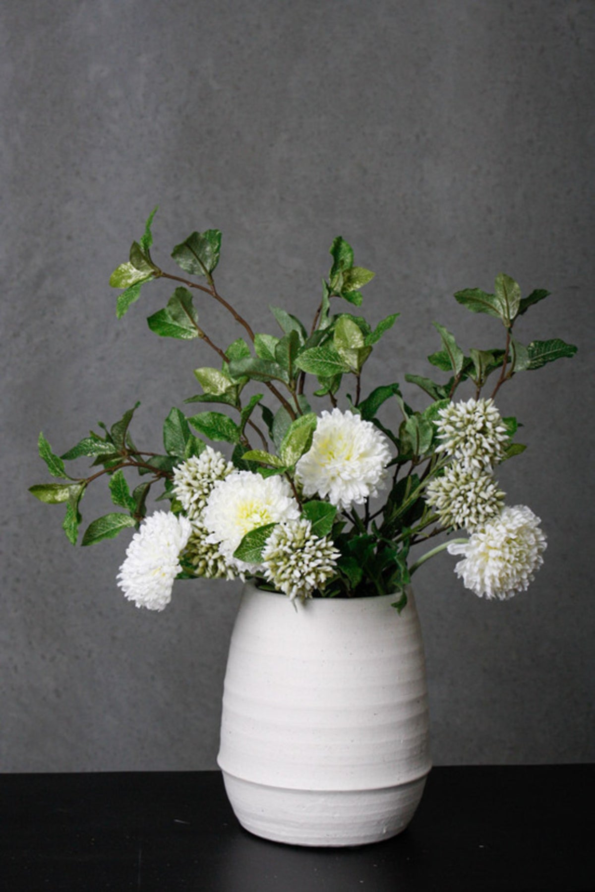Pittosporum leaf sprays arranged in a white vase against a dark wall