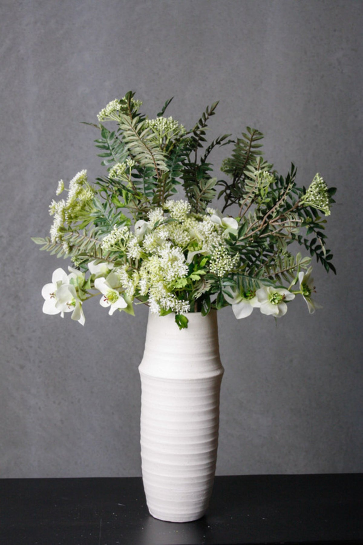 Rowan branches with green leaves styled in a white vase against a dark wall