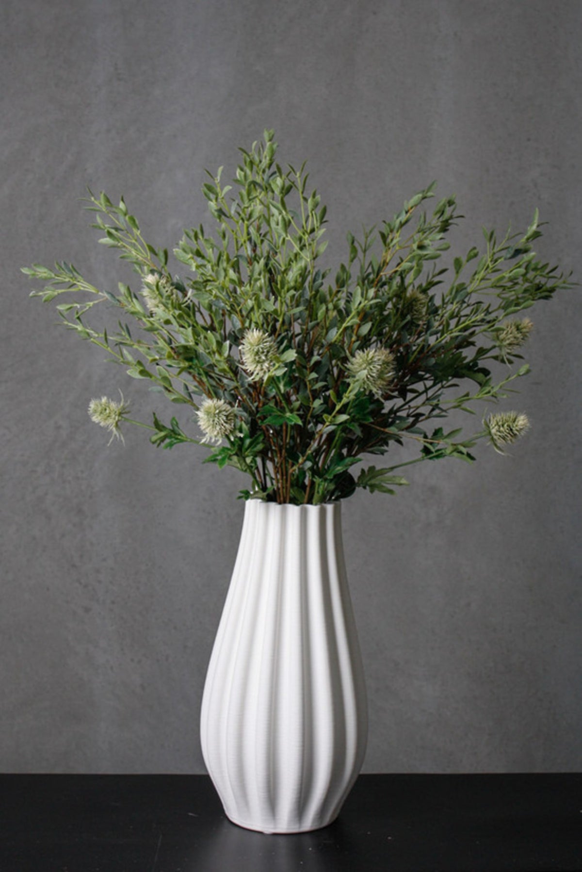 Italian ruscus sprays styled in a white ribbed vase against a dark wall