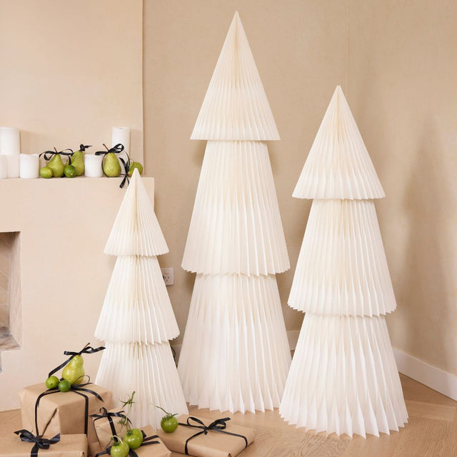 Three beige paper Christmas trees styled with wrapped gifts in a warm room