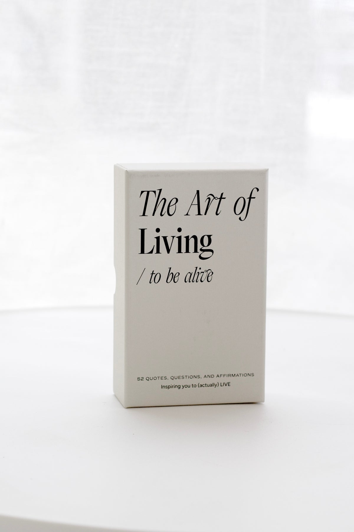 The Art of Living card deck box standing on a white table, soft window light behind