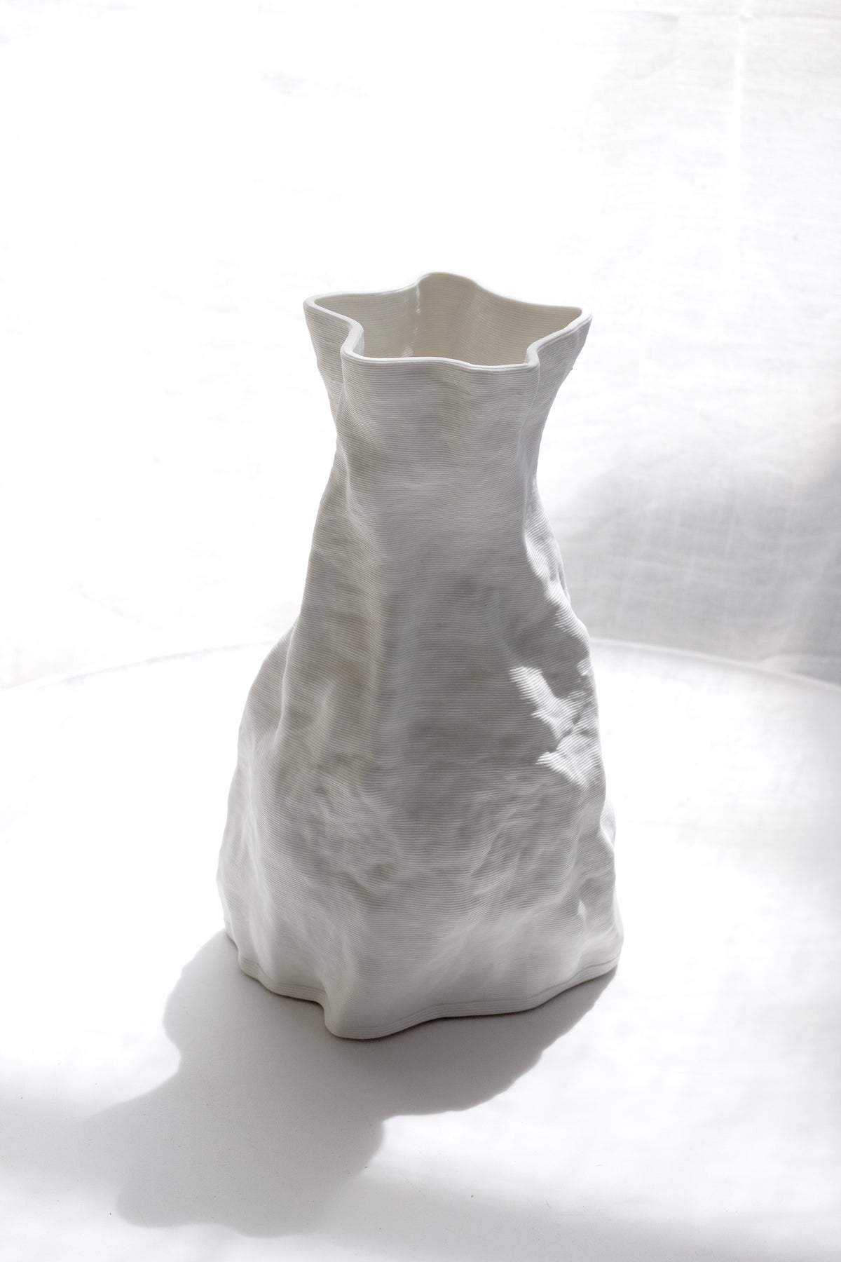 Zoe vase standing against a pale draped backdrop, folds catching the side light
