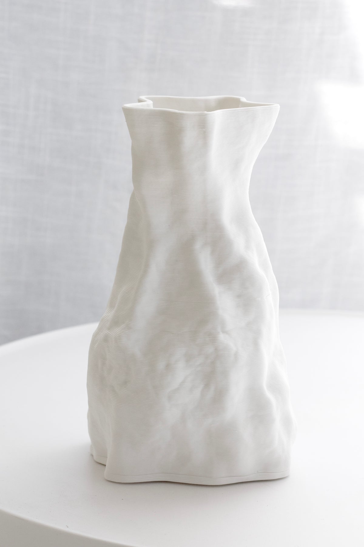 Zoe vase on a round white table with a linen curtain behind, shadow to one side