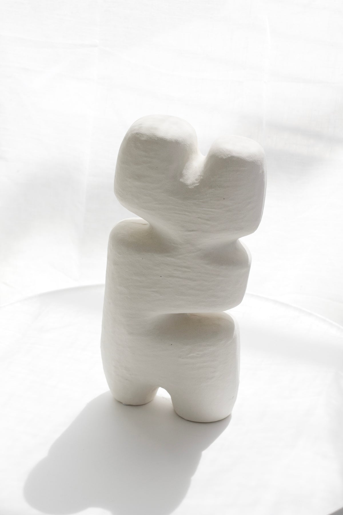 Block sculpture standing on a white curved surface, shadow stretching behind