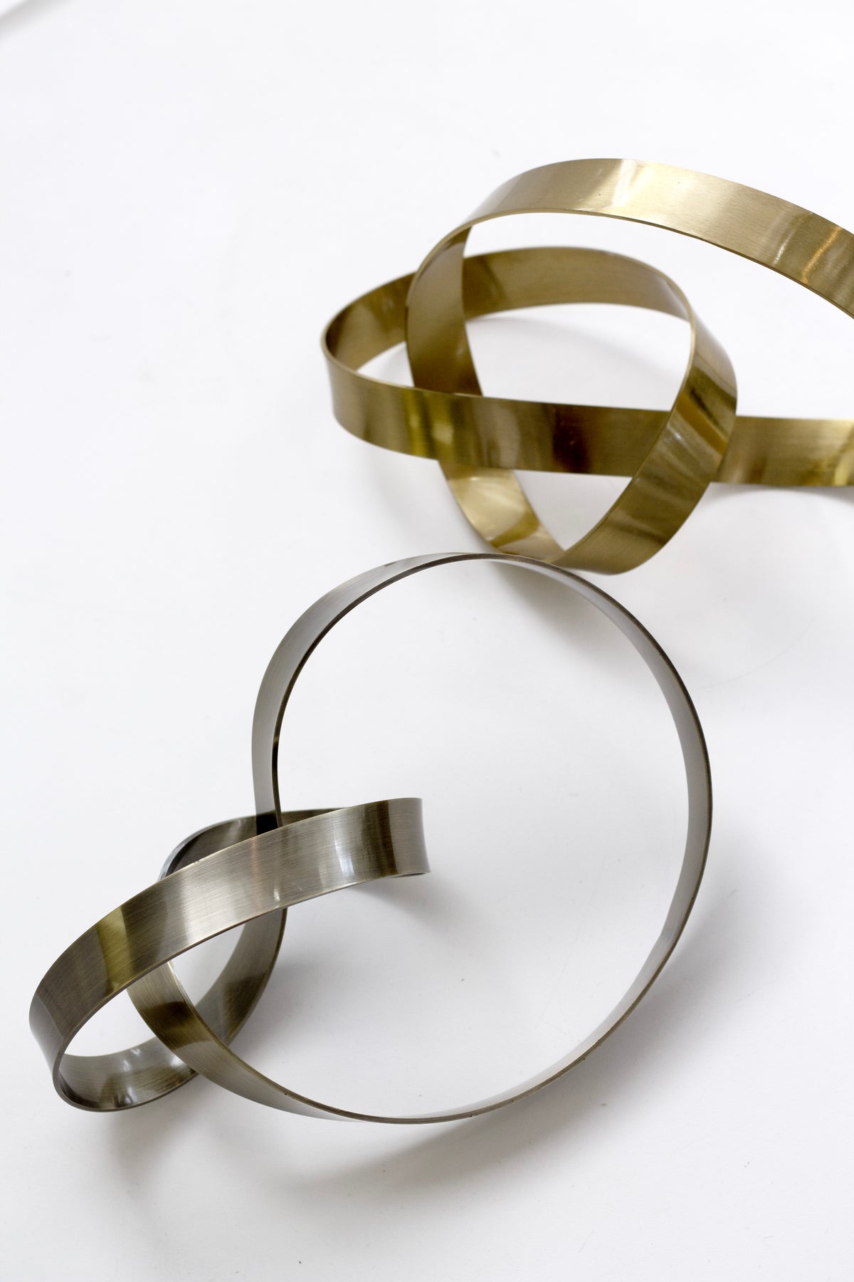 Gold and bronze Infinity Loop sculptures resting together on a white surface