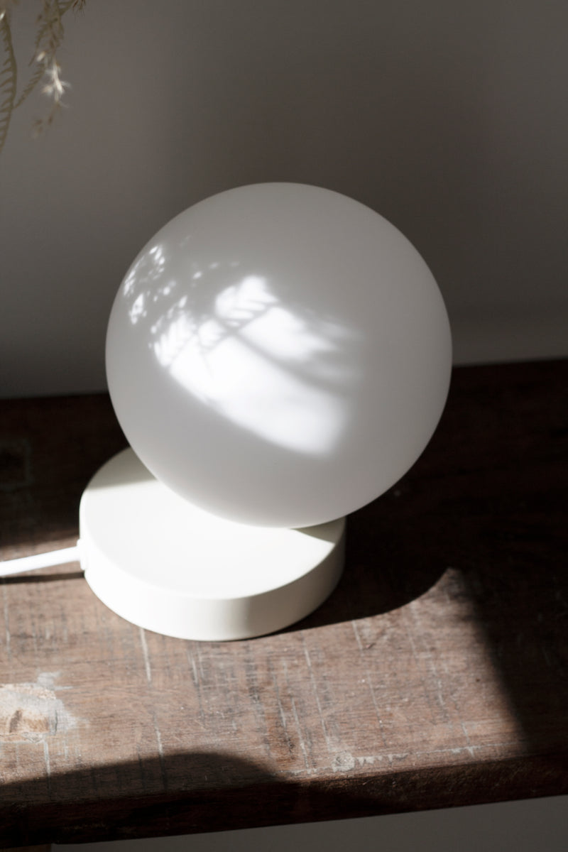 An elegant Yuri Table lamp from Ned Collections, with soft glow, sitting on a wooden table.