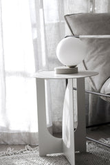 A white Yuri Table lamp from Ned Collections, softly glowing with LED bulbs, next to a couch.