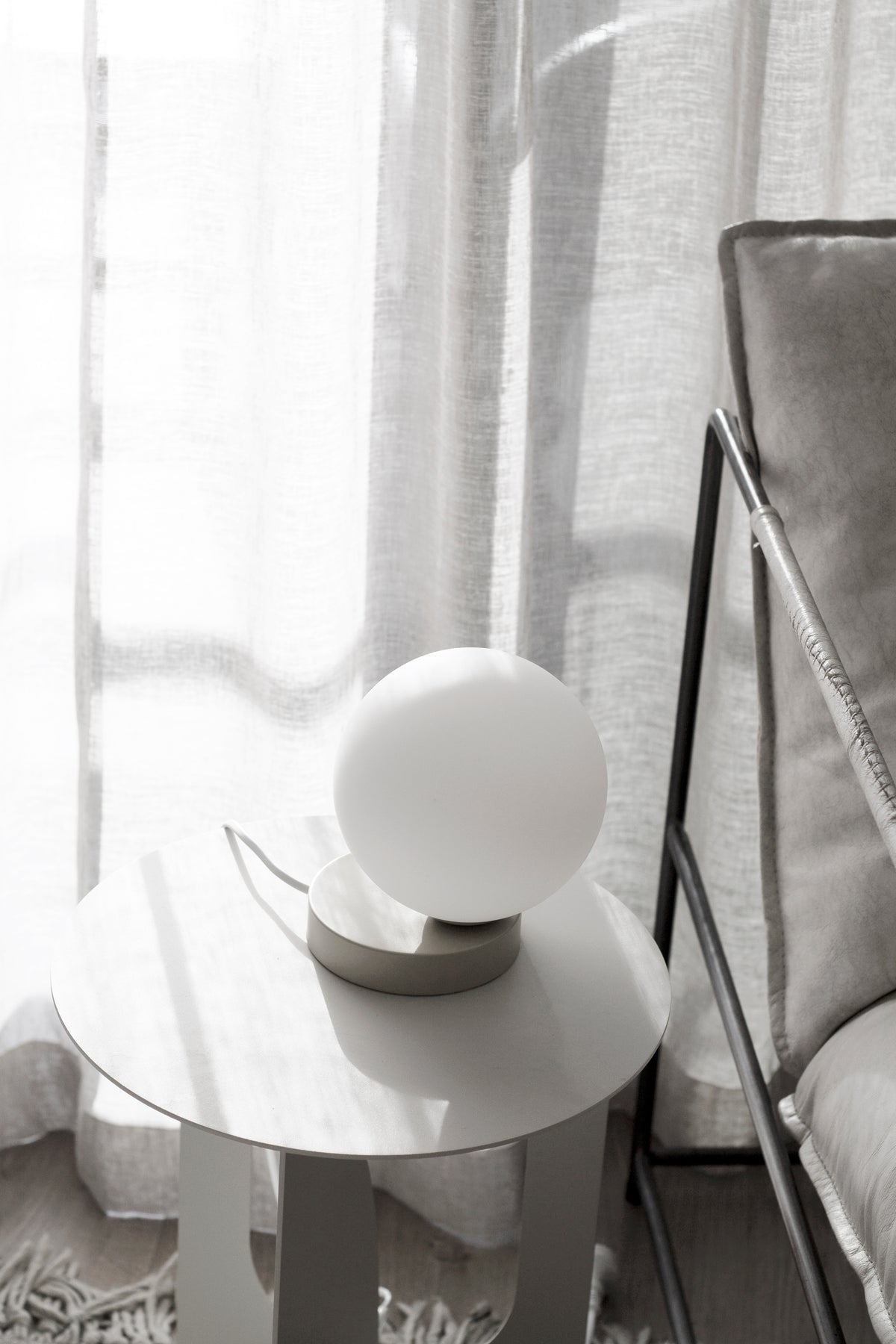 Yuri Table Lamp glowing on a round white side table by sheer curtains