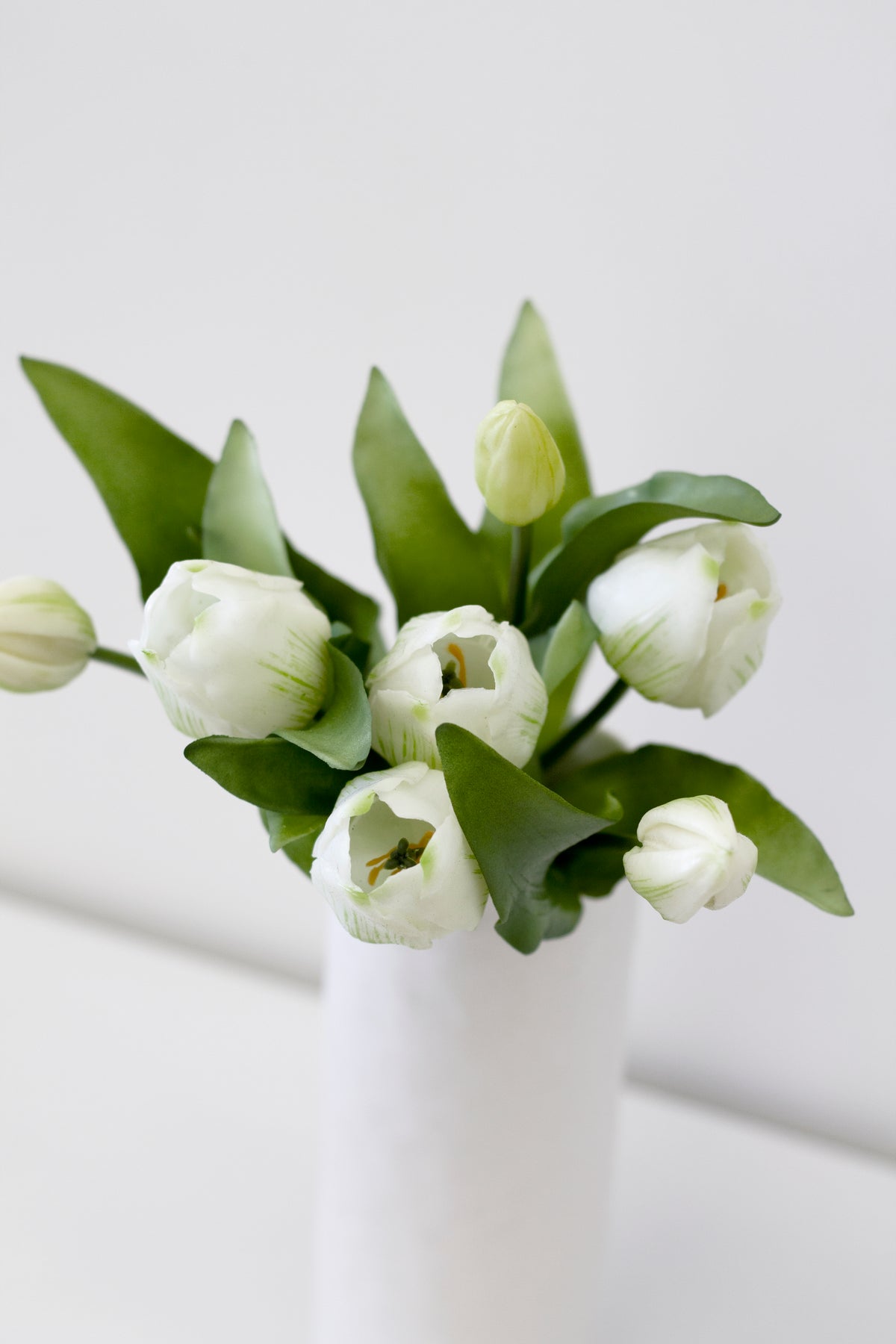 White faux tulips in a white vase on a pale table