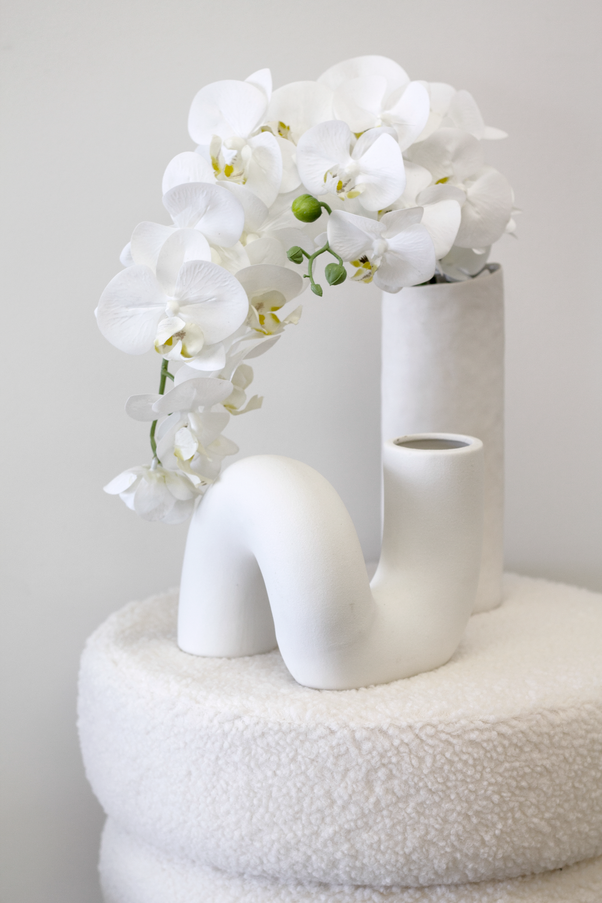White orchids in slim vases arranged on top of the white boucle ottoman