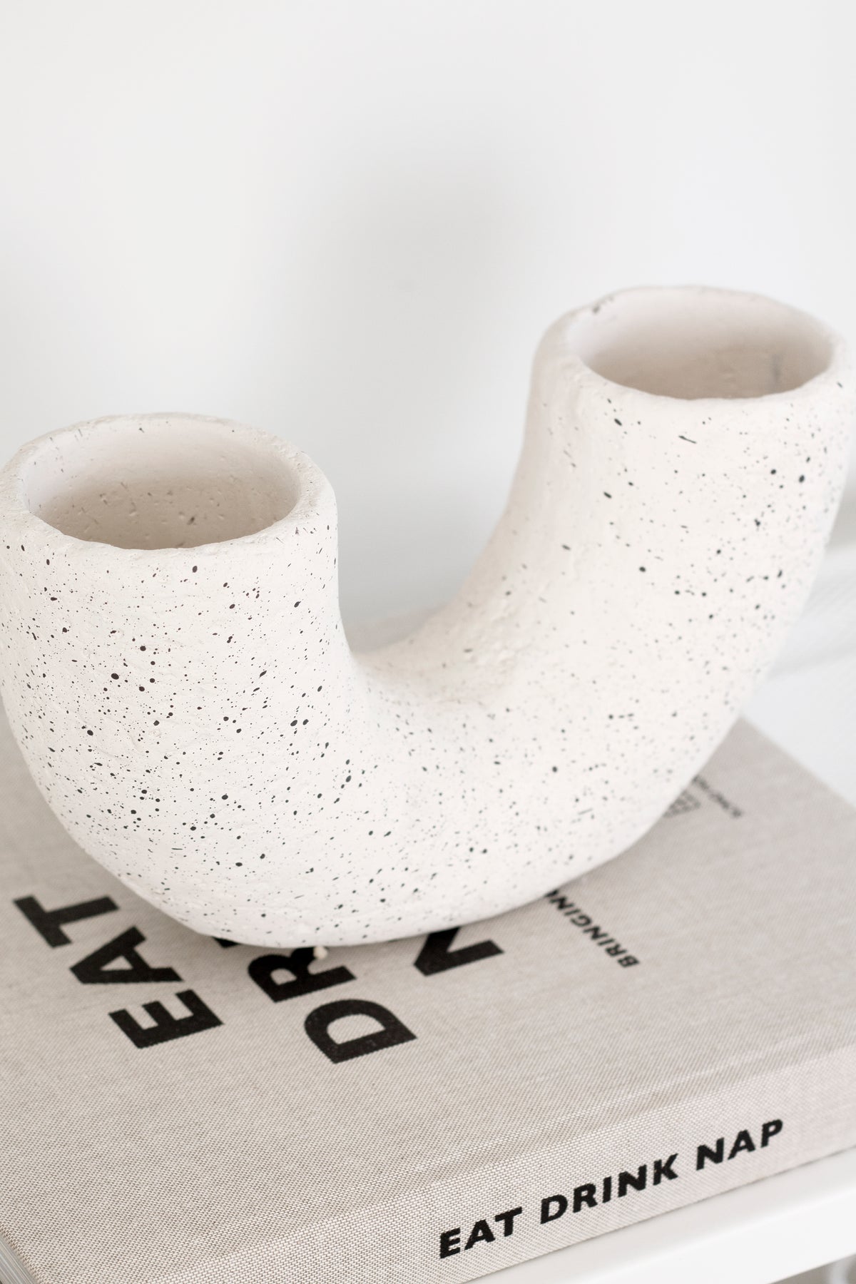 Curved white speckled vase beside the Eat, Drink, Nap book