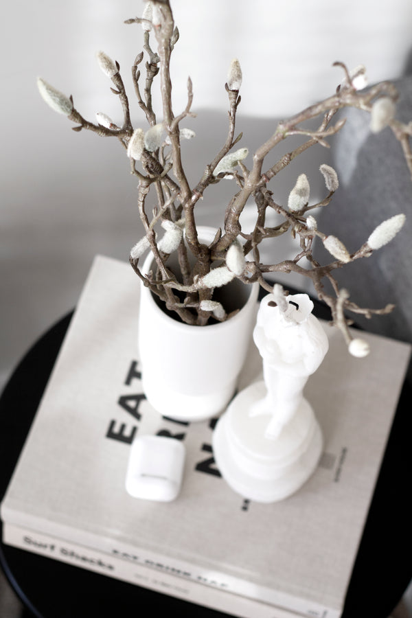 A white vase on a table adorned with Artificial Flora's Magnolia Branch next to a book.