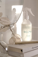 A bottle of Ecoya Laundry | Linen Spray is sitting on a table next to a clock.