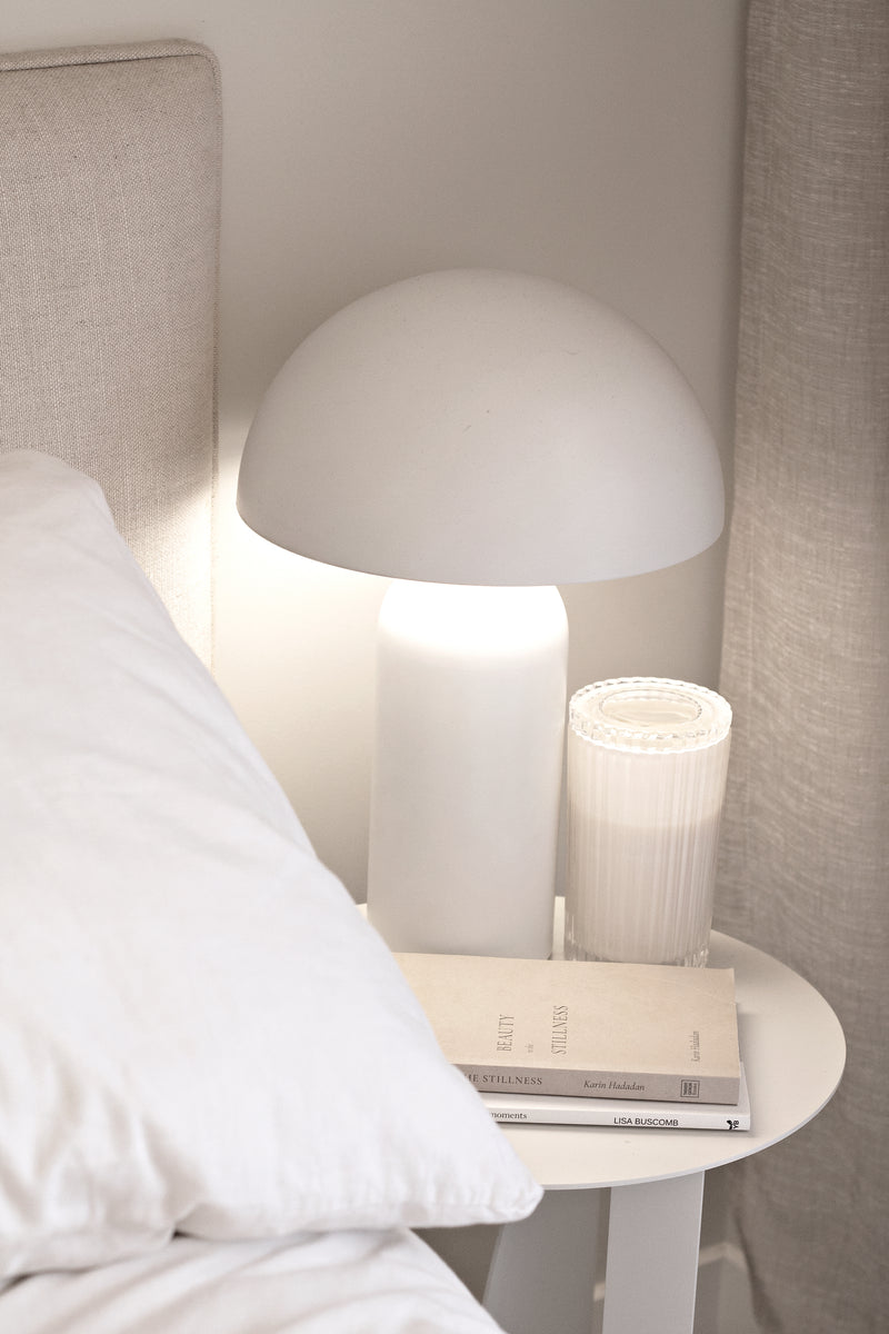 A white bed adorned with a Thought Catalog Beauty in the Stillness lamp on top, radiating beauty in the stillness.