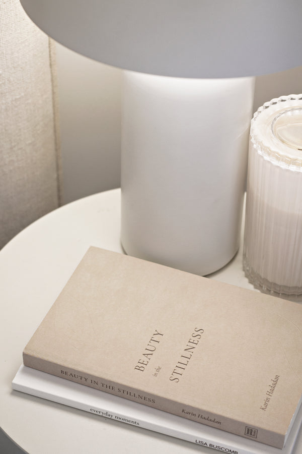 A "Beauty in the Stillness" book by Thought Catalog on a table next to a lamp, exuding timeless stillness.