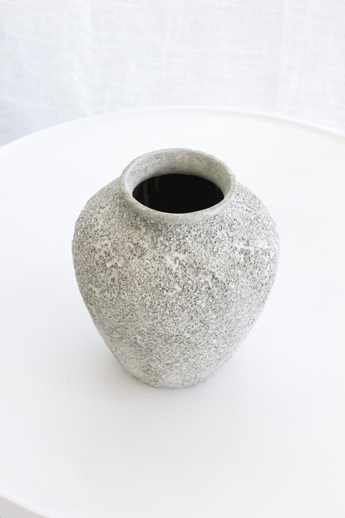 Small Nerina sage vase on a round white table against sheer curtains