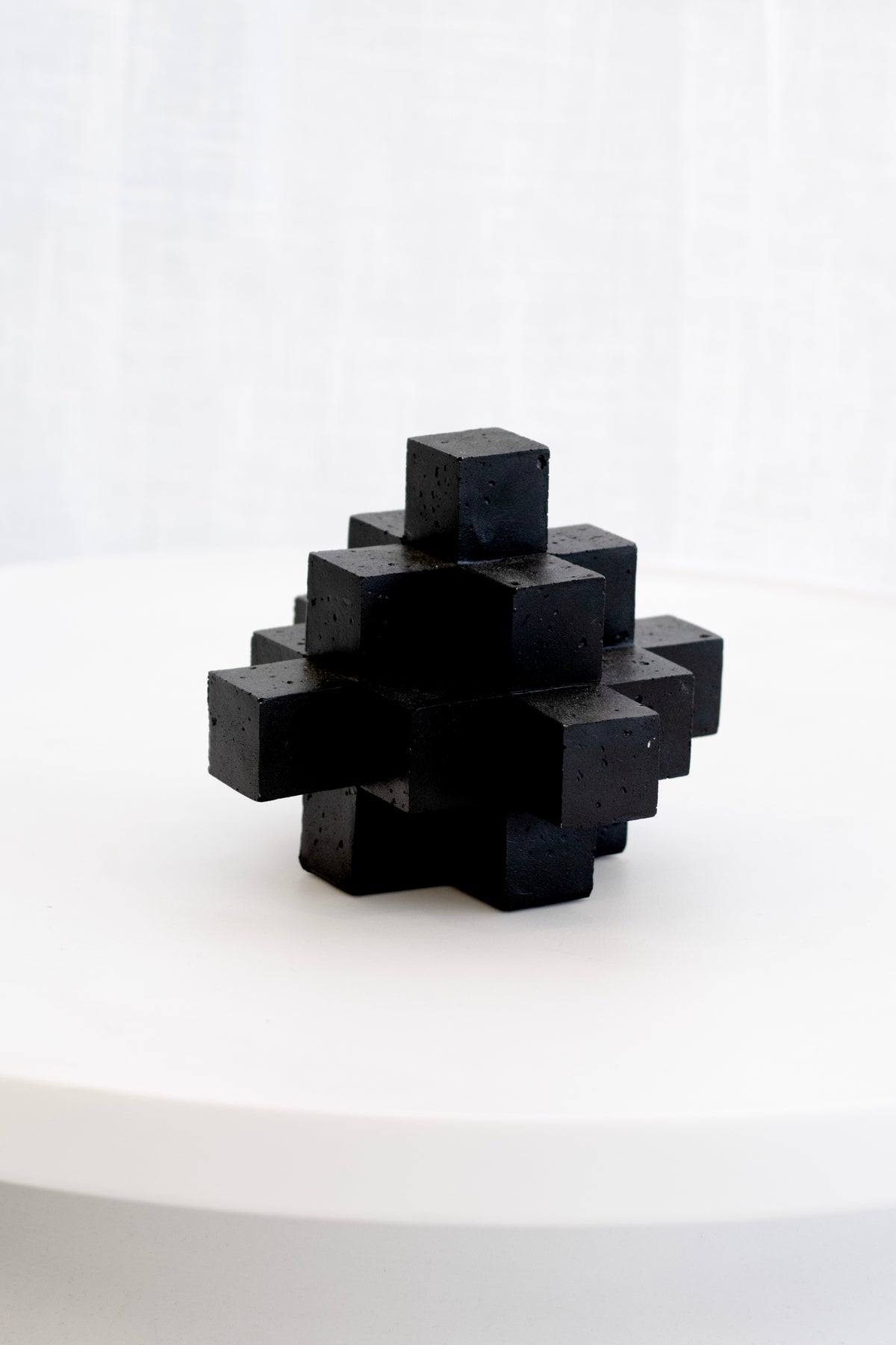 Black Cubism sculpture on a white pedestal against a sheer curtain
