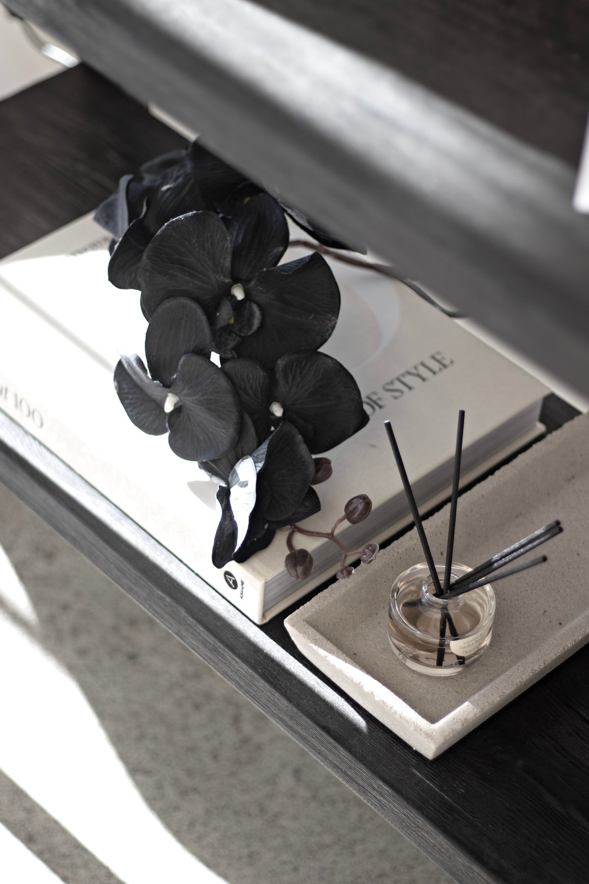 Black orchid on a book beside a diffuser on a dark table, close view