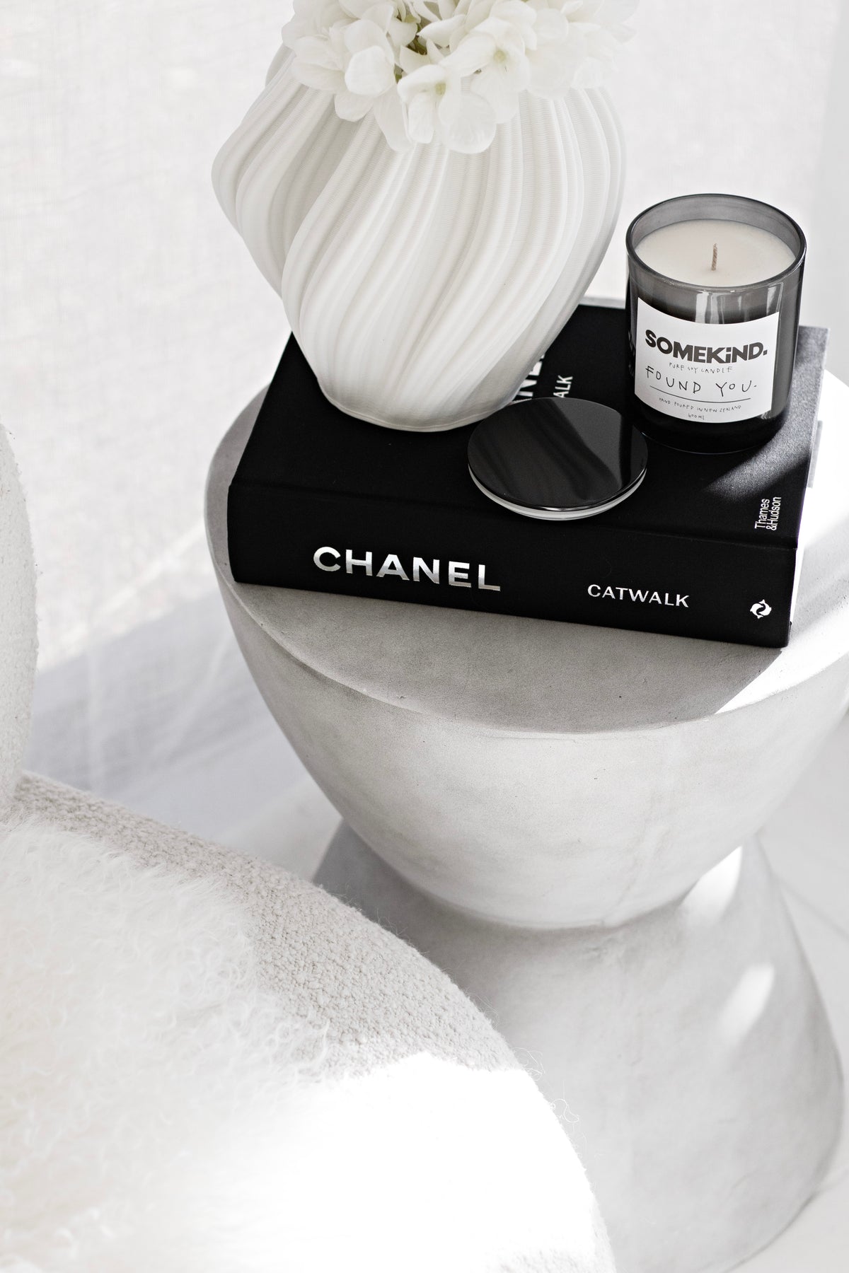 White Amelie fluted vase with a white bloom on a plaster plinth beside a candle on black books