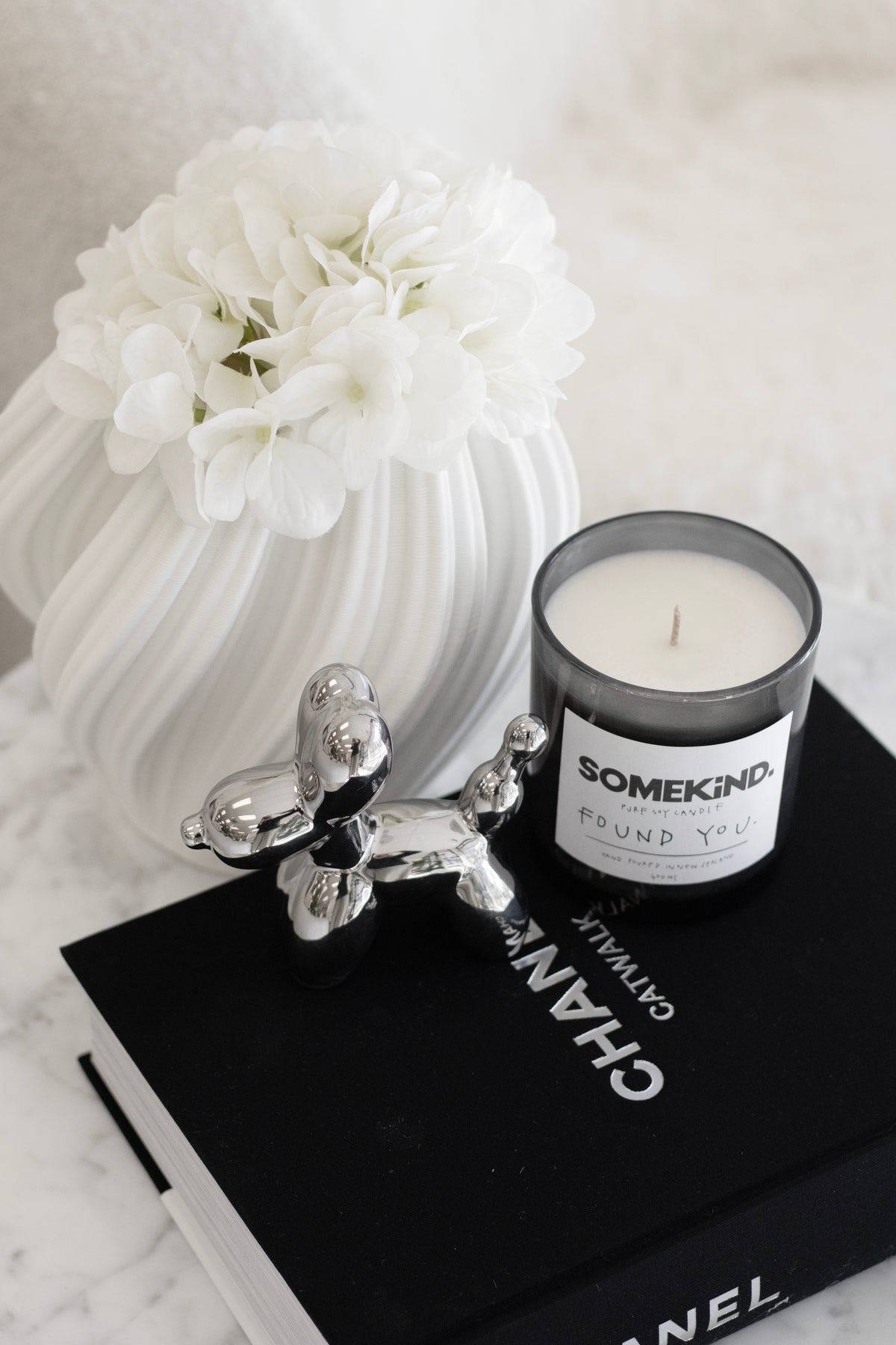 White Amelie fluted vase with a white dahlia beside a candle on black stacked books