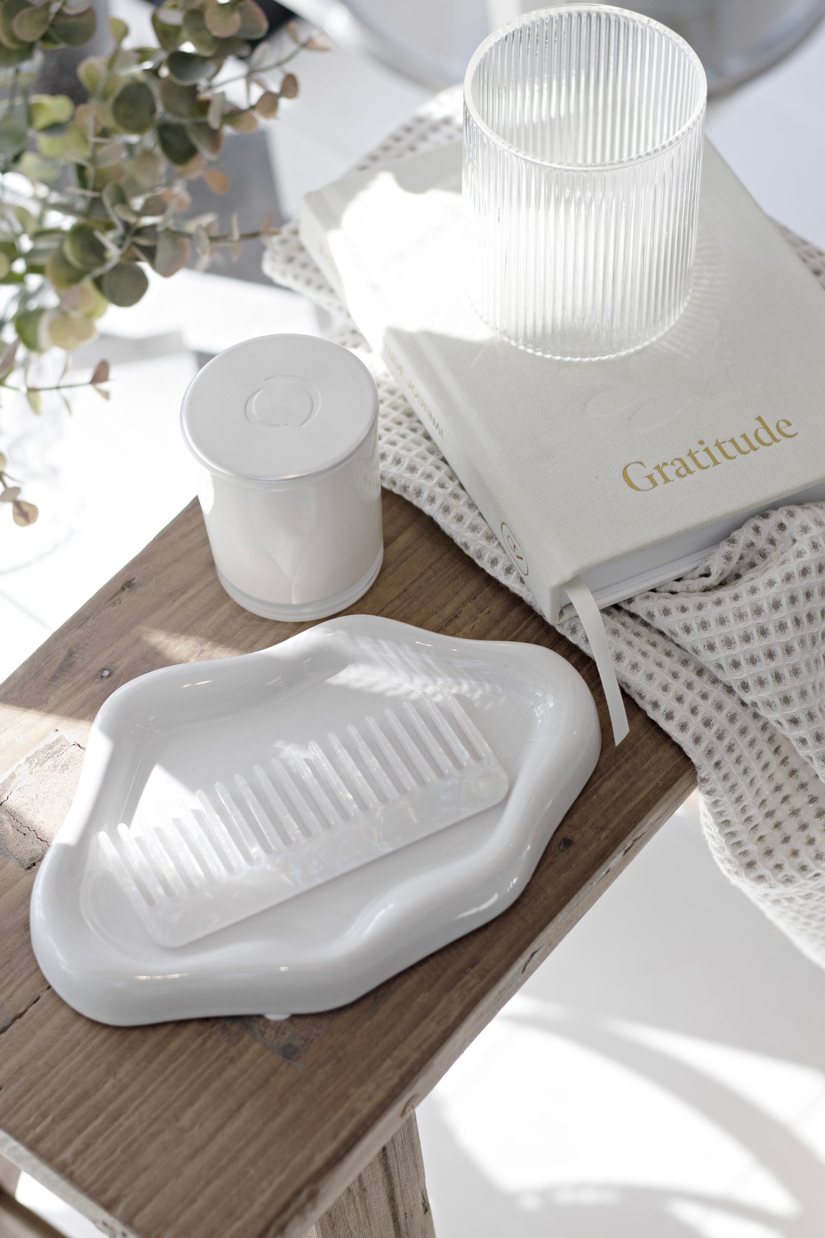 Gratitude journal beneath a white candle and ceramic dish on a timber surface