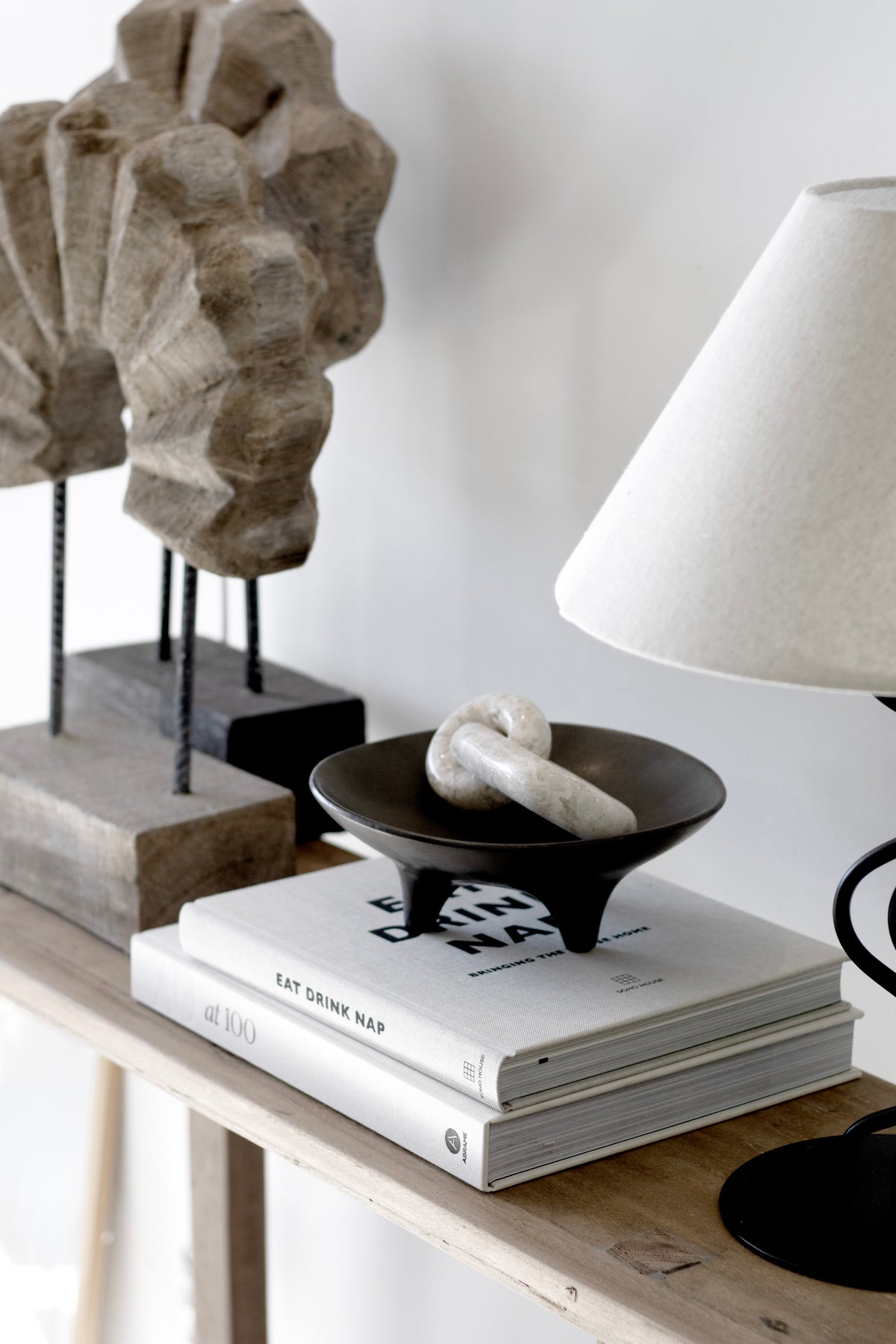 Onyx tripod plate on a timber console between a stone sculpture and a domed white lamp