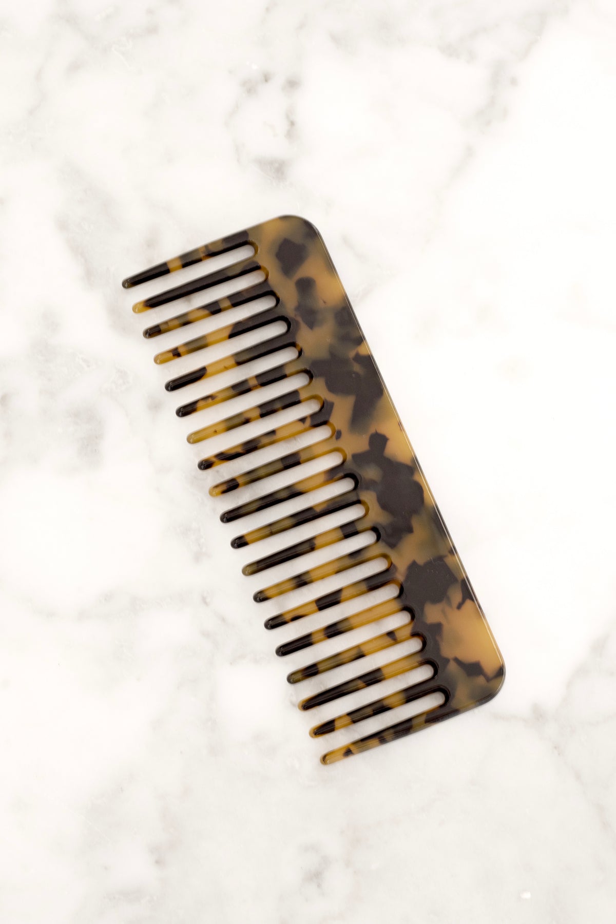 Dark tortoiseshell acetate comb on a marble surface, seen from above