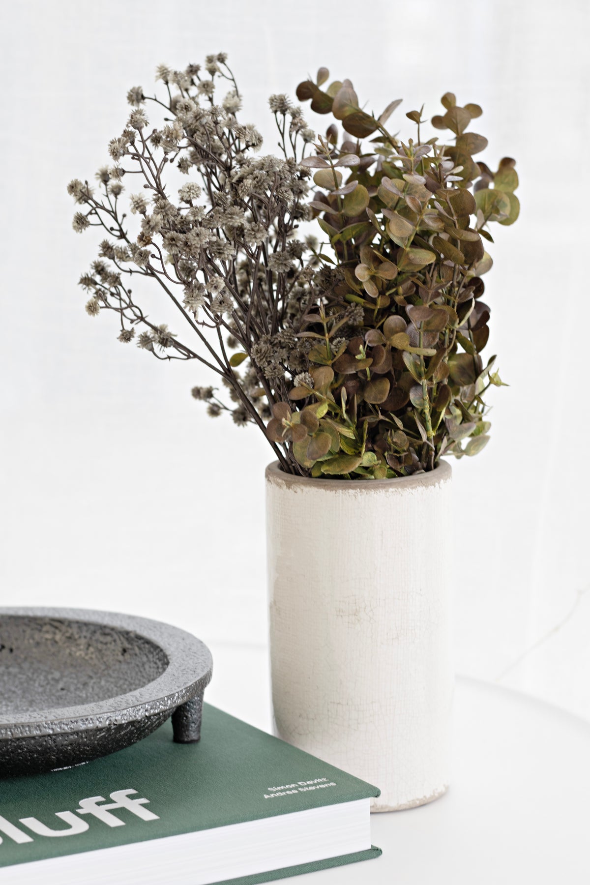Friars cement tripod plate on a green book beside a cream vase of dried foliage