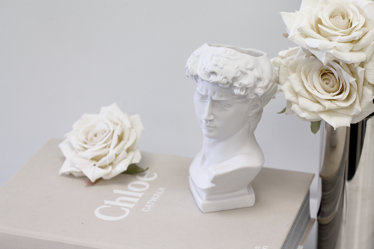 Champagne roses in a silver vase beside a white bust and a single loose rose