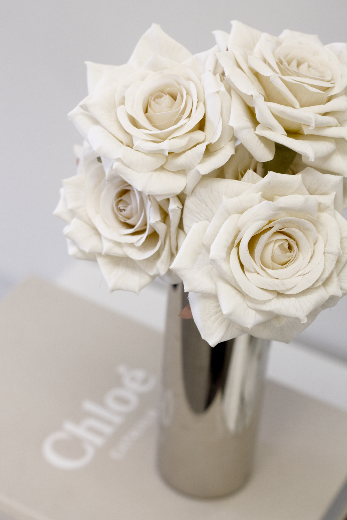 Champagne roses in a tall silver vase on a white coffee table book