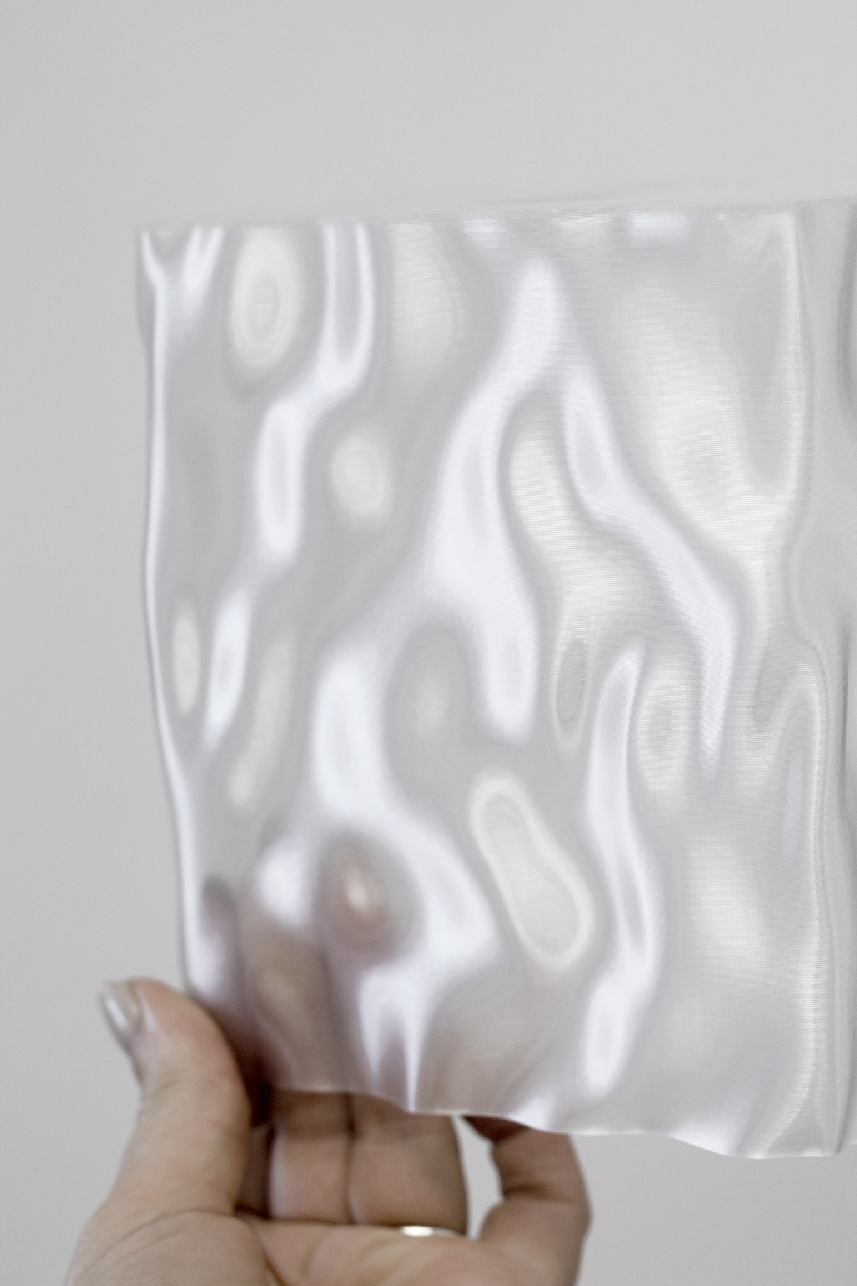 Hand holding up a clear Flow cover to show its wave pattern against the light