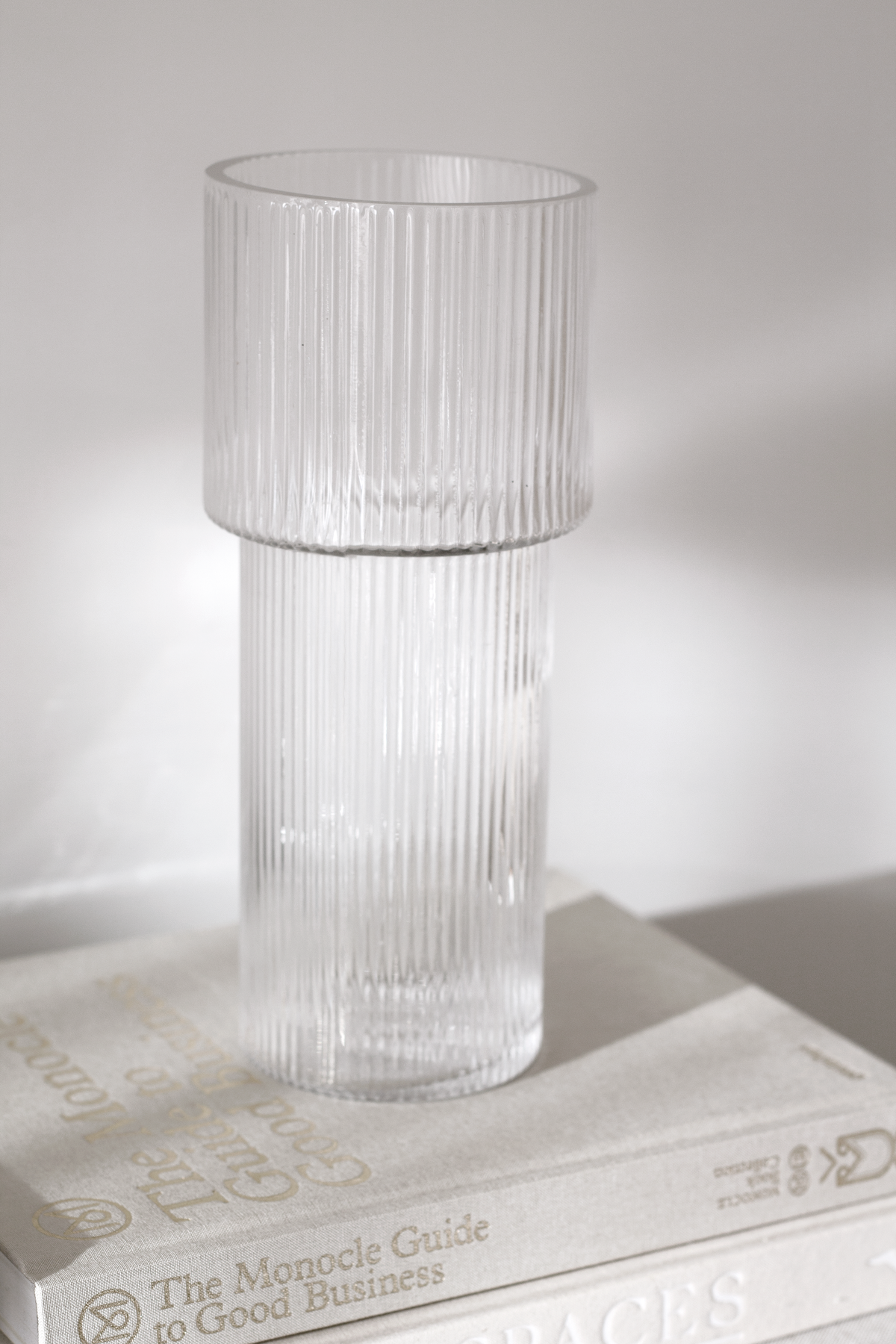 Ribbed glass vase standing on a stack of books against a white wall