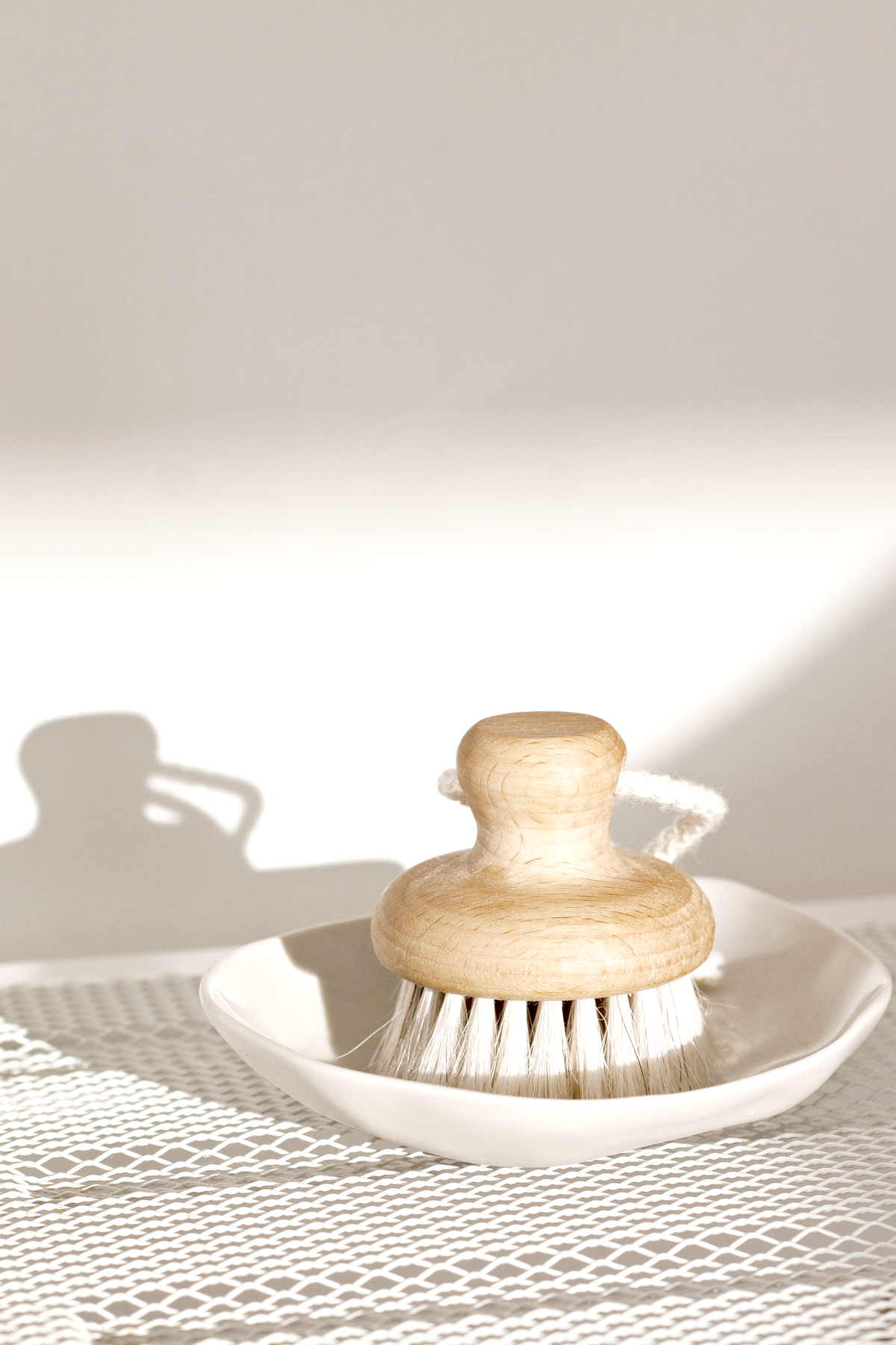 Natural goat hair face brush with a wooden handle displayed on a white ceramic dish in soft morning light, creating a serene and minimal skincare setting.