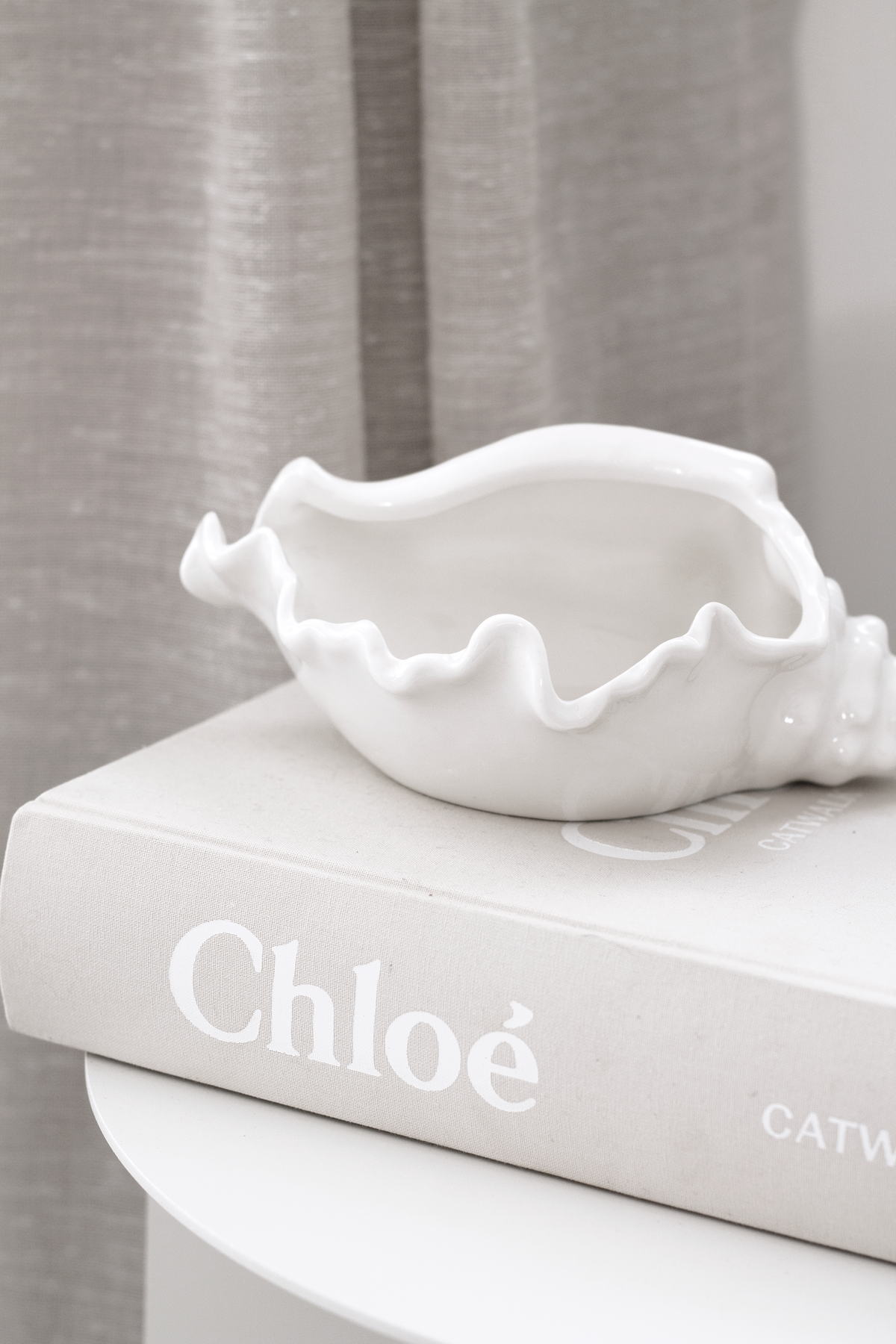 Conch bowl on a large format book, textured grey curtains behind
