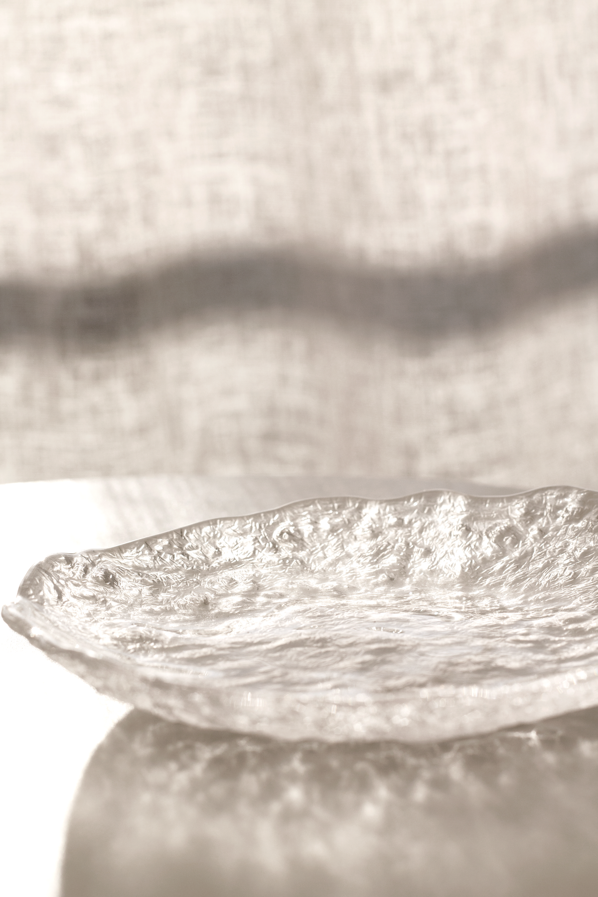 Glacier glass tray on a pedestal from a low angle against linen