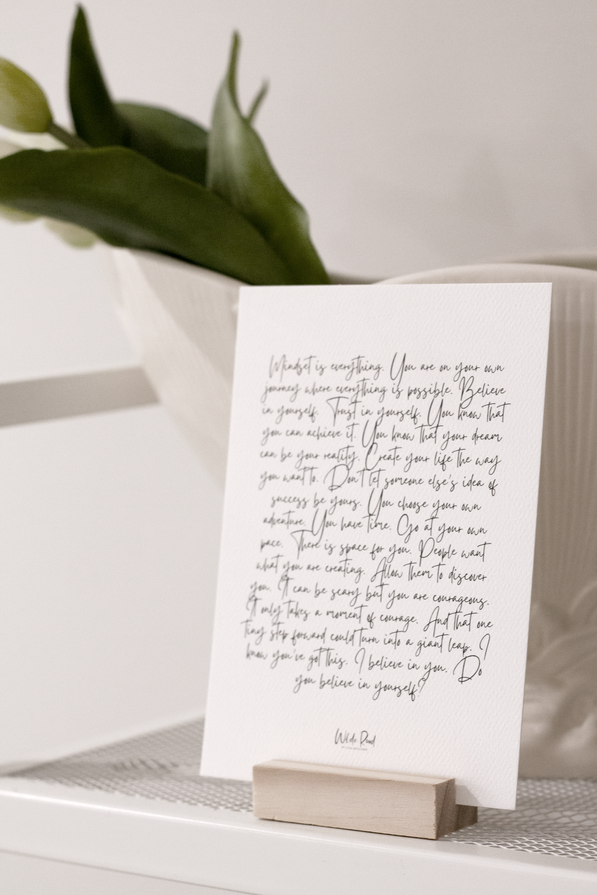 Affirmation card on a wooden stand beside a green leaf