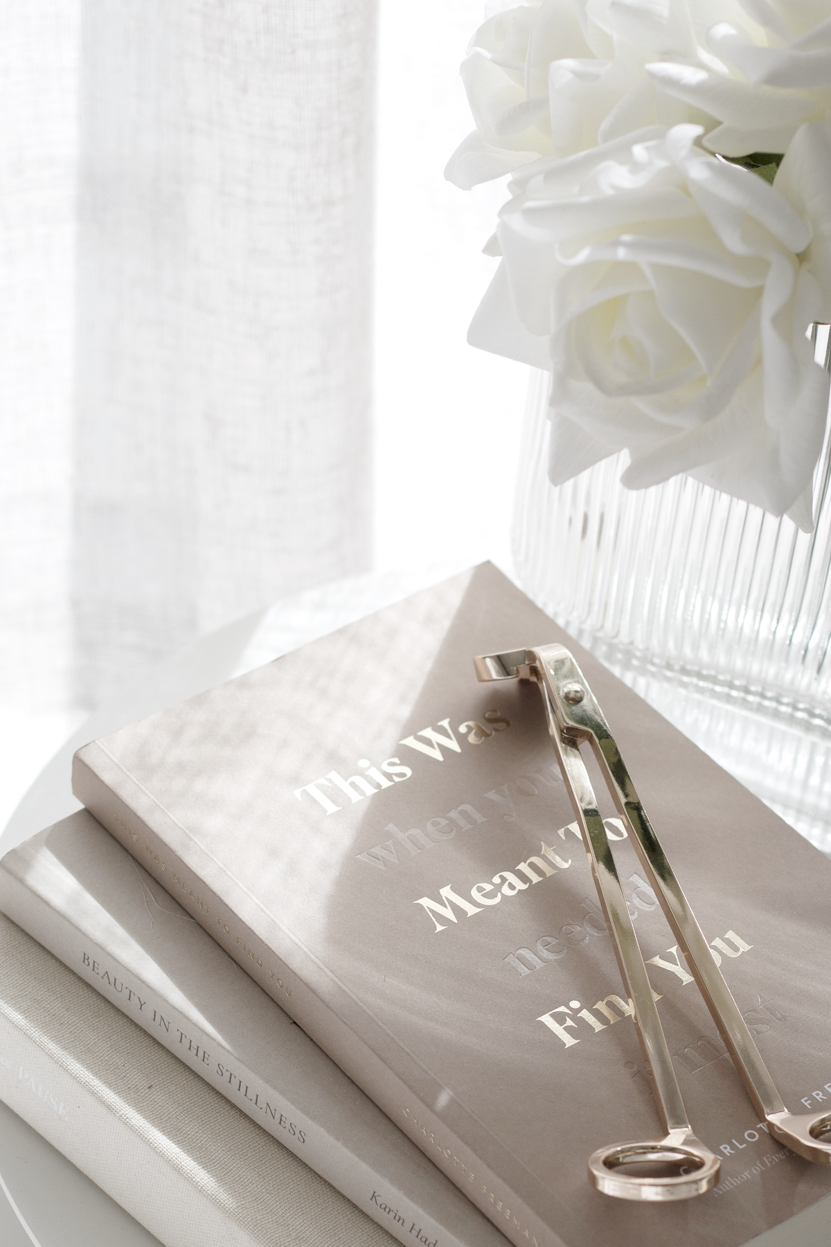 Soft neutral poetry book with gold foil title styled with a candle wick trimmer and white roses in a ribbed glass vase.