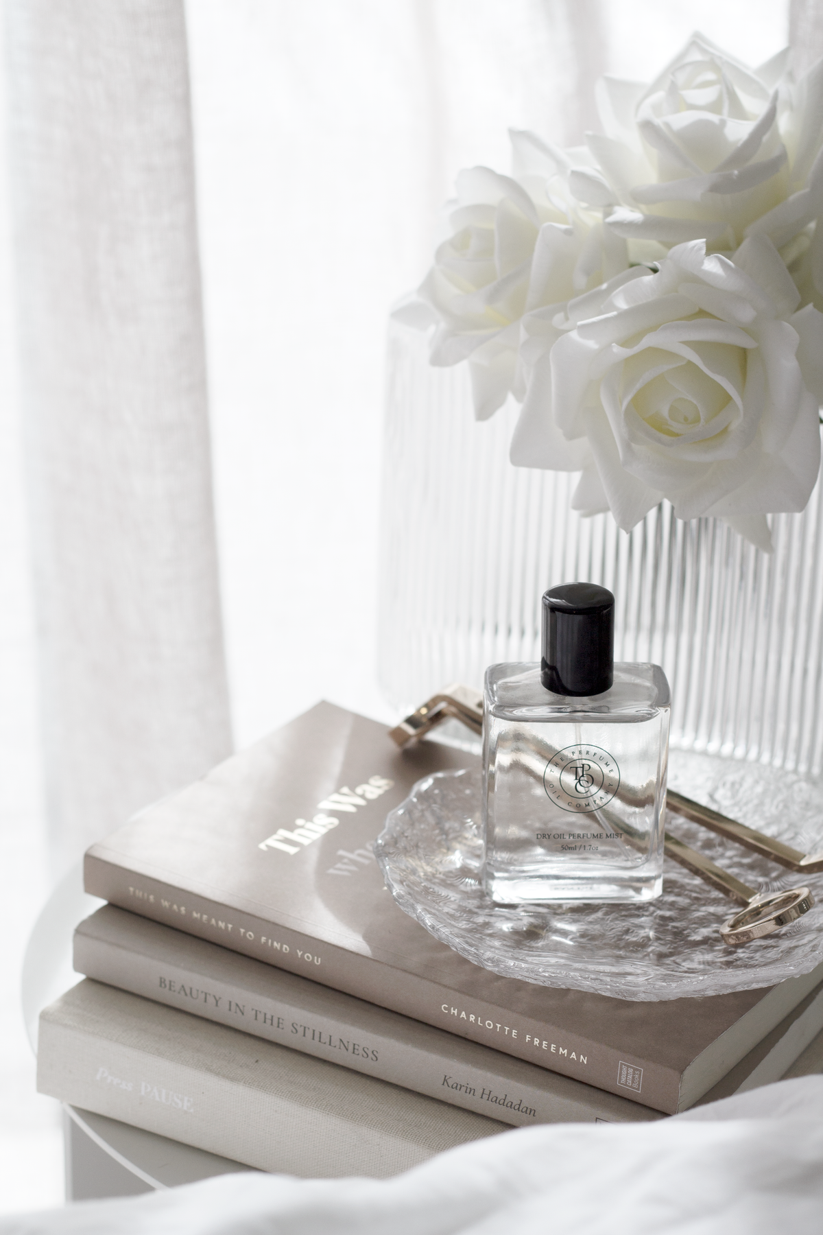Glacier glass tray with a perfume bottle on stacked books, white roses above