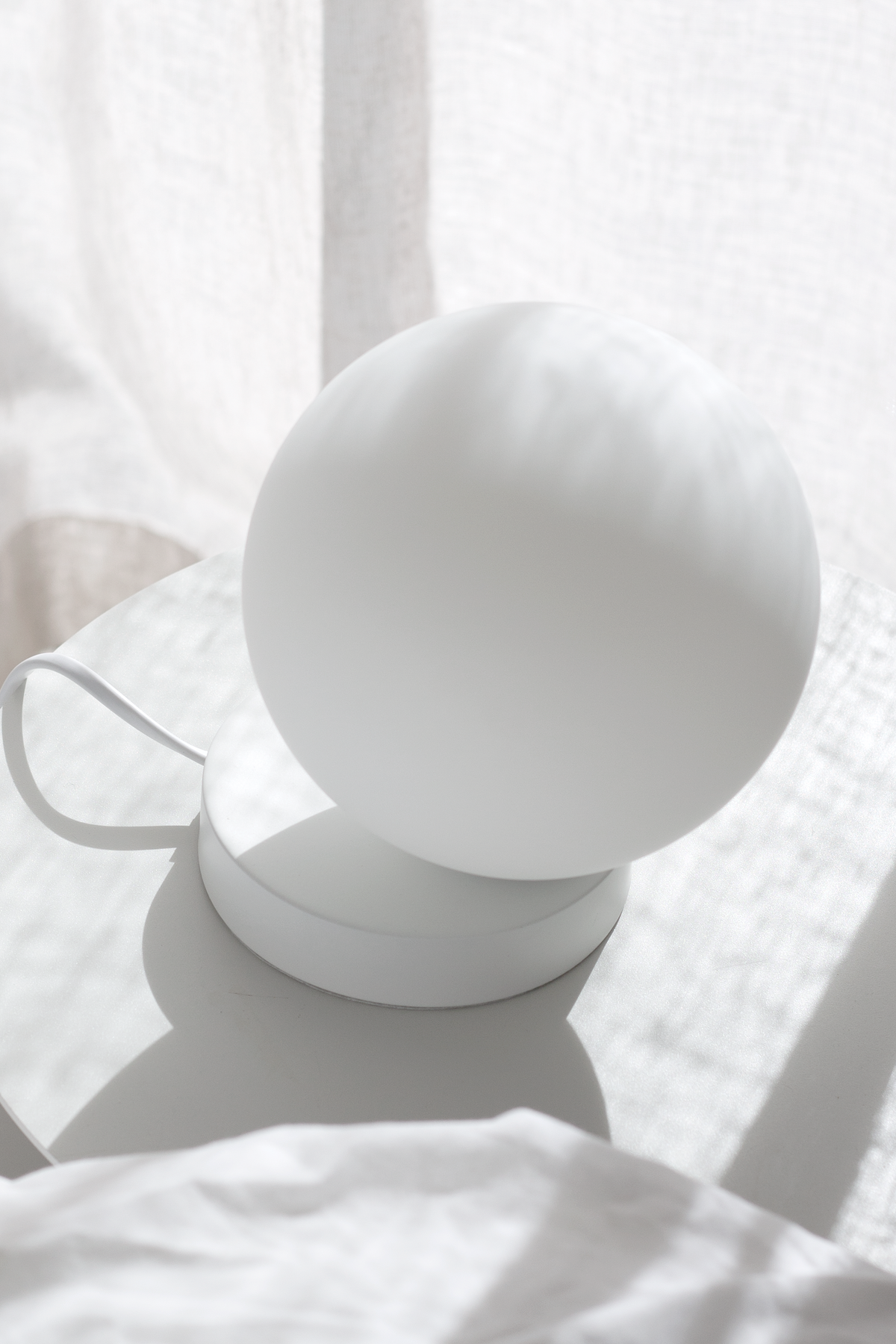 Yuri Table Lamp beside sheer curtains on white bedding in soft daylight