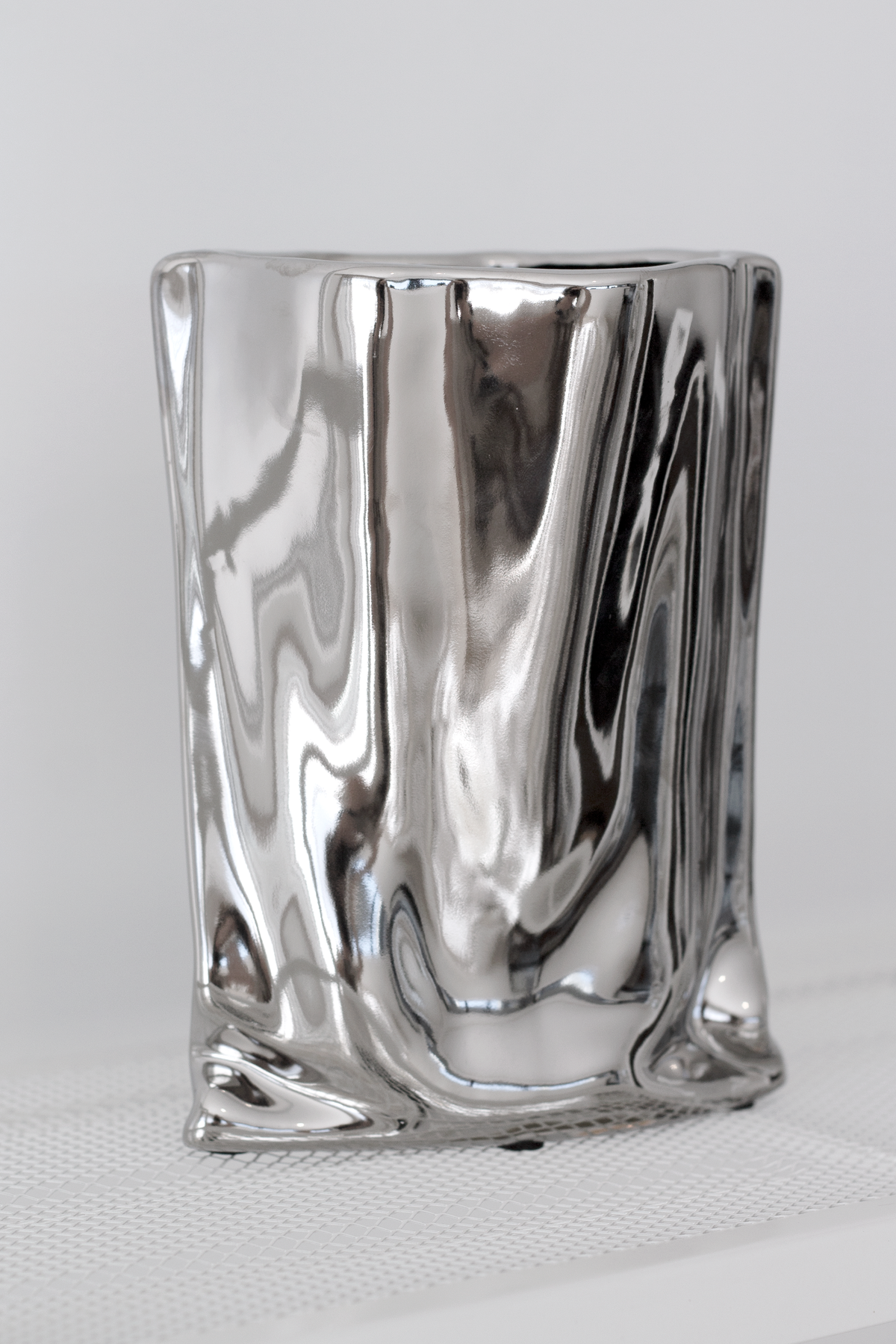 Silver metallic bag vase on a pale surface against a linen backdrop, front view