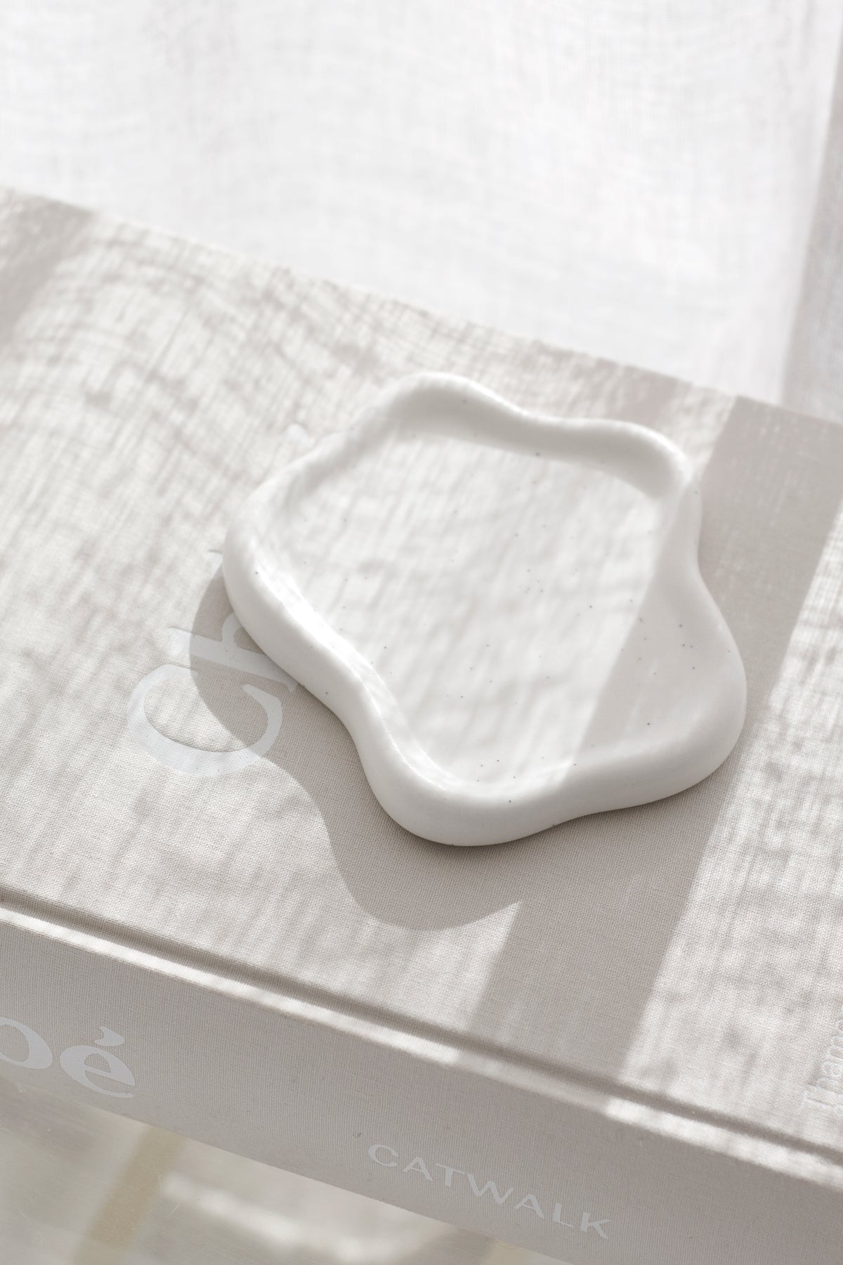Empty white cloud trinket dish on a glass table in soft light