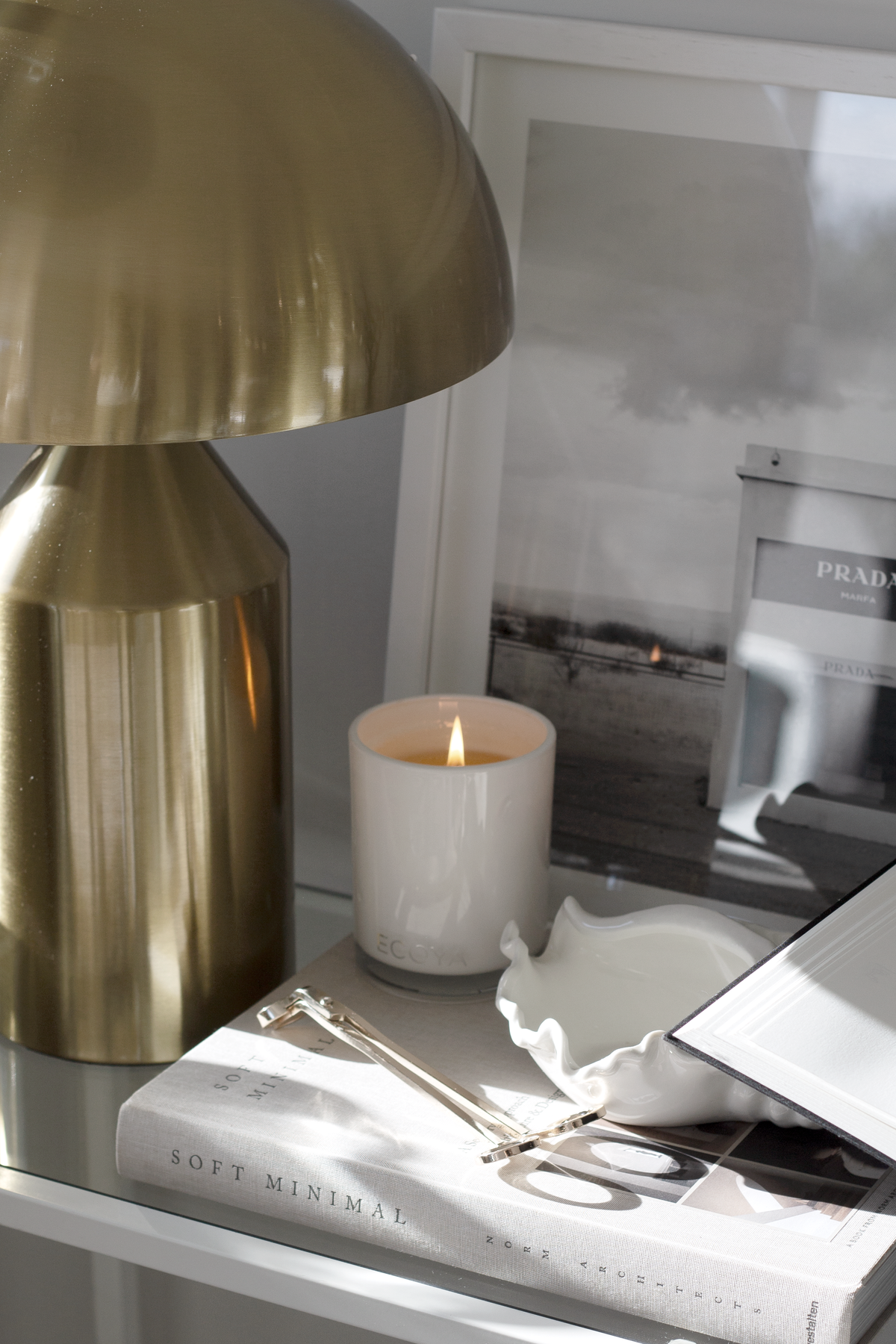 Gold wick trimmer on a magazine beside a lit candle and a brass domed lamp
